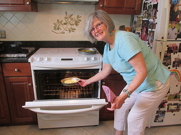 Woman smiling while pulling pan out of oven in kitchen