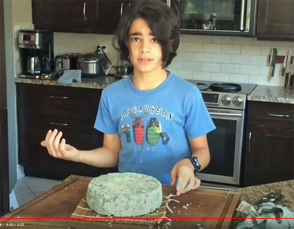 Girl standing in kitchen with block of cheese on cutting board