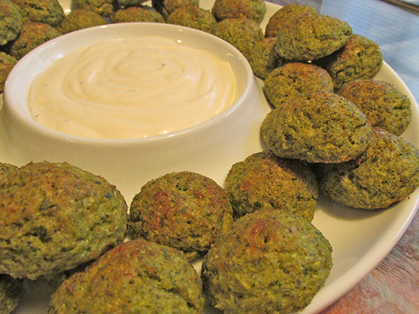 Dark green cookies sit on a platter with a white dipping liquid