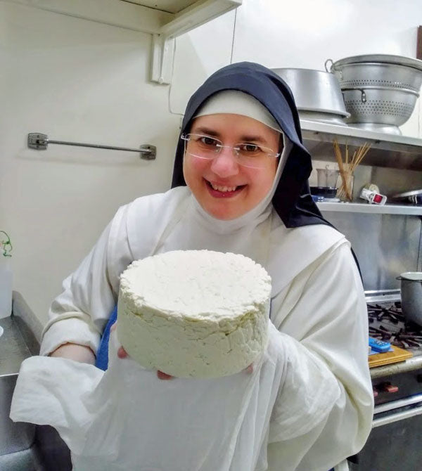 A nun holding a wheel of cheese.