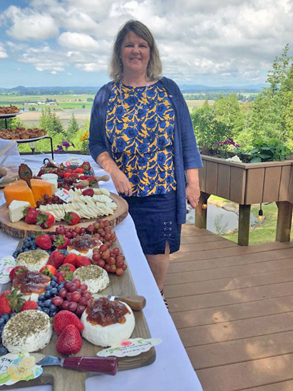 Woman standing next to table filled of fruit, cheese, and jelly