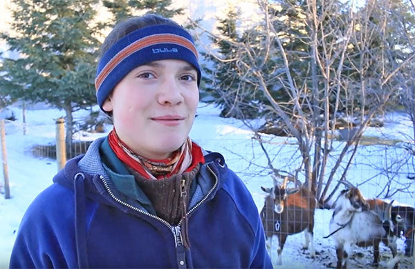 Boy standing out in the winter with goats in background