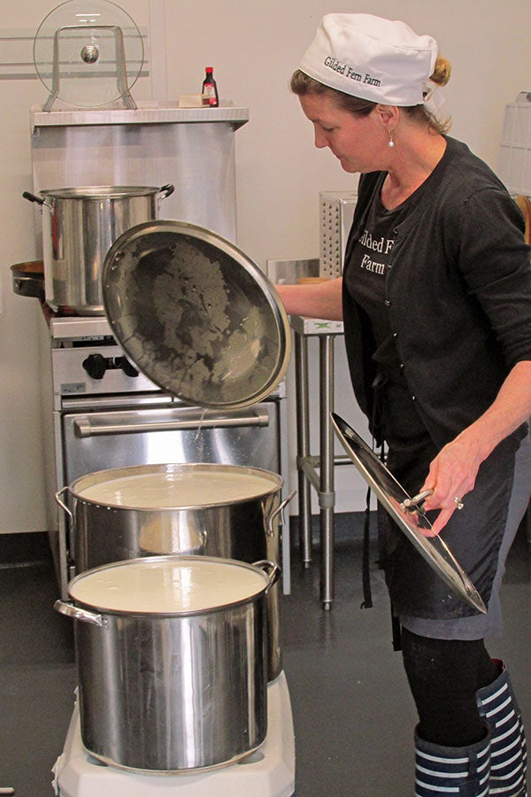 a woman lifting lids off metal pots full of cheese