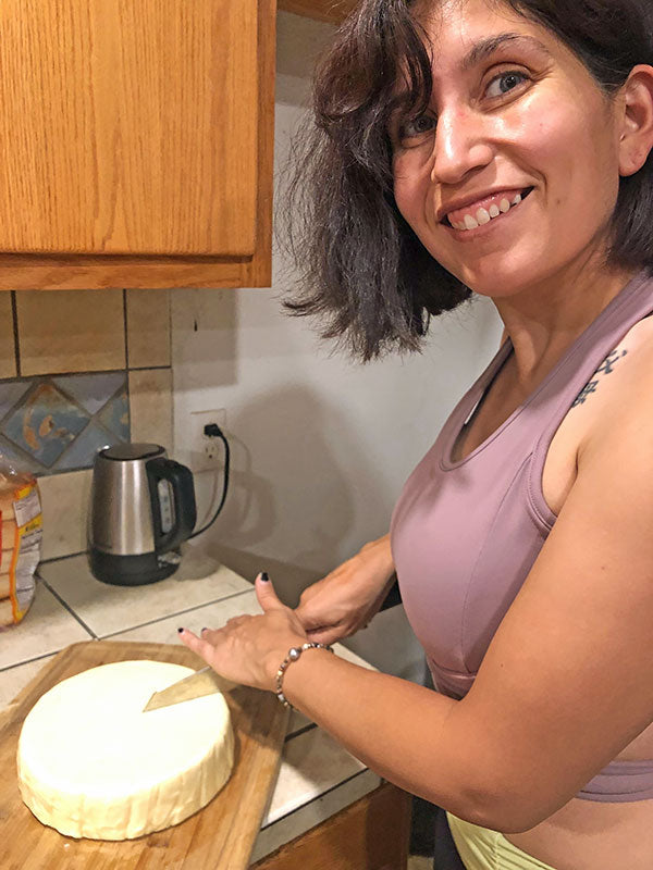 Woman cutting block of cheese on cutting board on counter