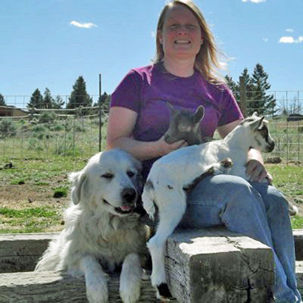 Woman with baby goats on lap and dog next to her