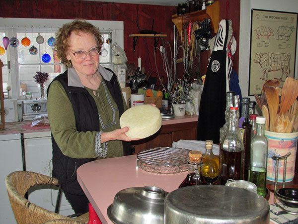 A woman holding a wheel of cheese in a kitchen