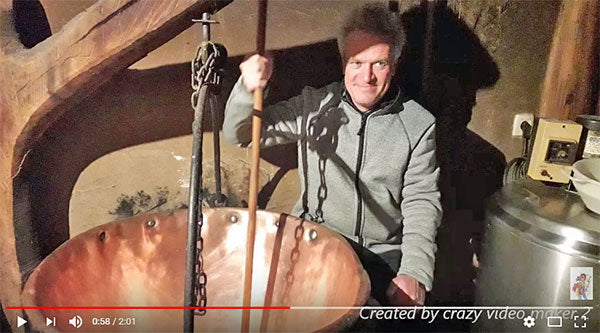 A screenshot of a man stirring something in a large copper vat